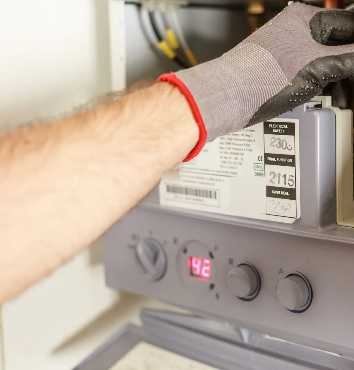 Gloved hands working inside an open wall-hung boiler above its control panel