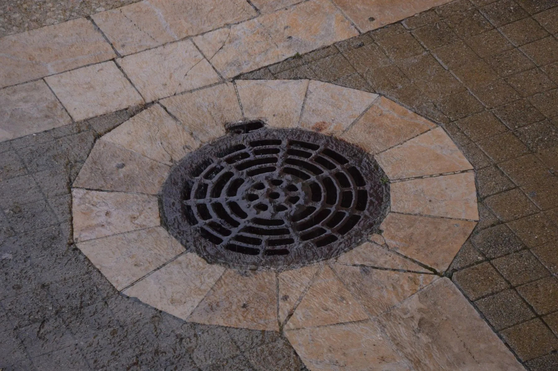 A round cast iron drain cover set into sandstone paving