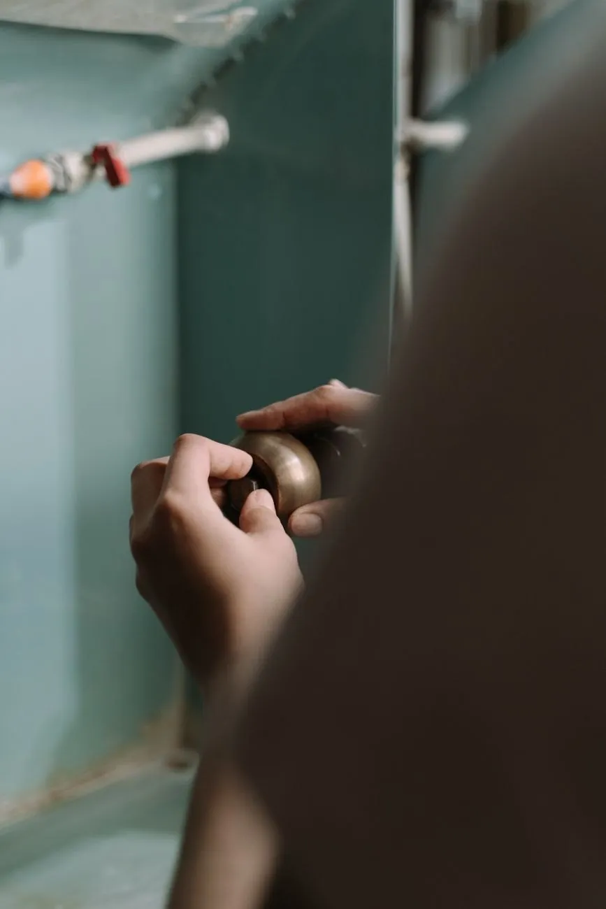 Hands fitting a brass nut on pipework inside a sink cabinet
